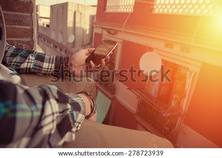 Brave man sitting on the edge of the roof with mobile phone in his hand (intentional sun glare)