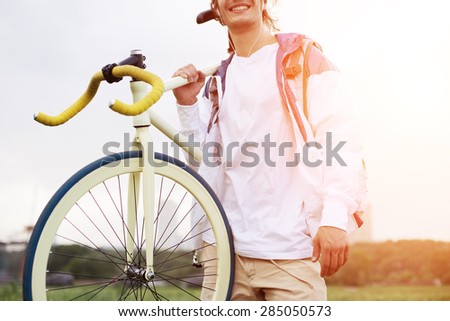 young man in blank t-shirt standing with bicycle on his shoulder  at sunset (intentional sun glare and bright colors)