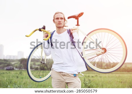 young long hair man in blank t-shirt standing with bicycle (intentional sun glare and bright colors)