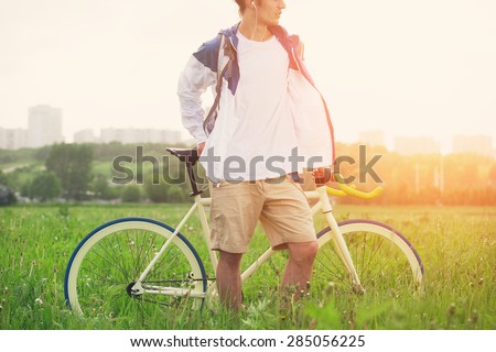 Man in blank t-shirt with bicycle standing in green field (intentional sun glare and bright color)