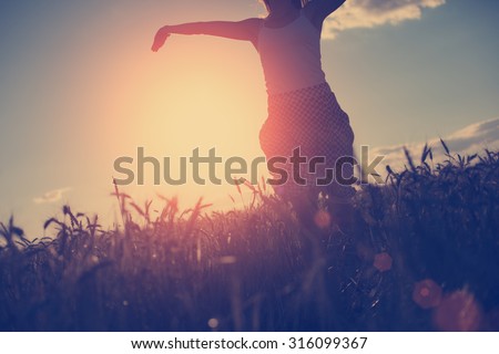 A girl in dress running and having fun in the evening in the field at sunset (intentional sun glare and vintage color, little motion blur)