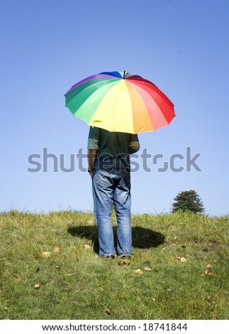 A person standing alone, watching the horizon, with a rainbow colored umbrella.