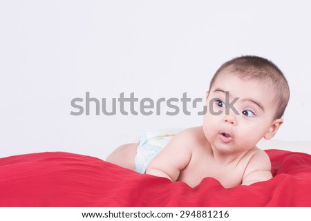 Curious baby with diaper looking with wondering eyes  while lying down on red sheet