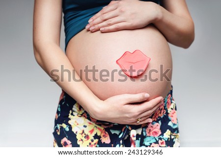 Closeup on tummy of pregnant woman, a cute pregnant belly. Plaque with the name of the child in the form of lips for text