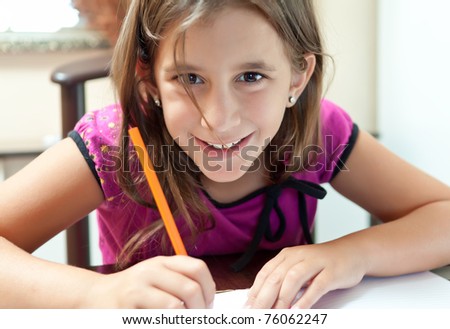 Beautiful small girl smiling at the camera and working on her school project at home