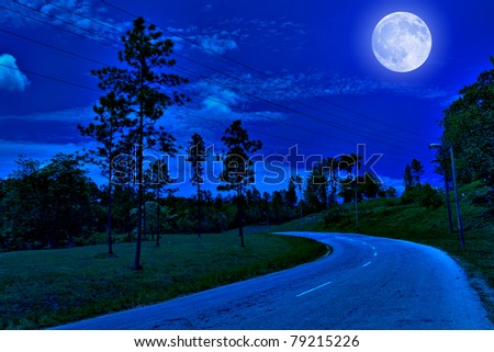 Lonely road in the country illuminated by a bright full moon at midnight