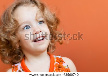 Portrait of a small girl with beautiful blue eyes smiling on a colorful orange background