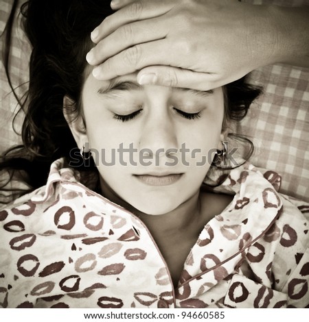 Desaturated sad portrait of a small girl sick with fever and a woman\'s hand touching her forehead