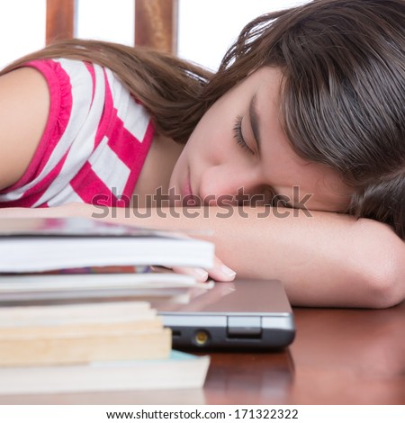 Tired female student sleeping over her laptop with a stack of books on the table