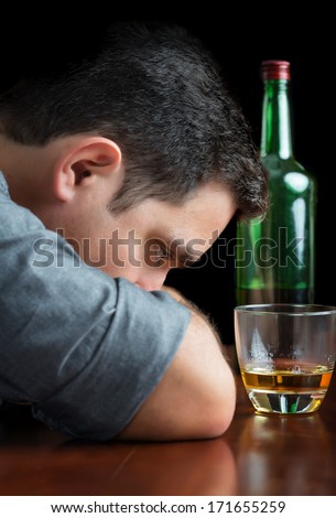 Depressed alcoholic man staring at a glass of scotch on a black background