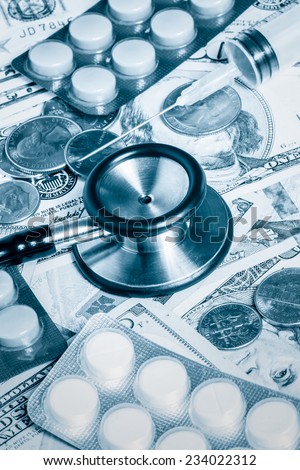 Health care cost - Stethoscope,pills and syringe over a stack of dollars toned in blue