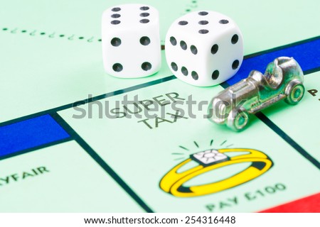 LONDON,UK - FEBRUARY 11, 2015 : Dice and token next to the SUPER TAX space in a Monopoly game board