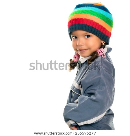 Funny mixed race small girl wearing winter clothes and a colorful beanie hat isolated on white