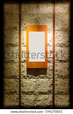 Blank wooden frame on stone wall illuminated spotlights in interior room (with strong vignette)