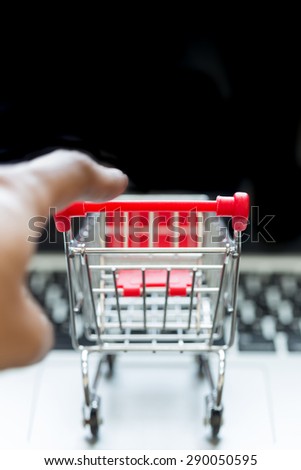 Selective focus : Mini red shopping cart on laptop with human hand for shopping online concept