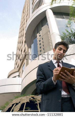 A business man standing in front of a building writing in his day planner.