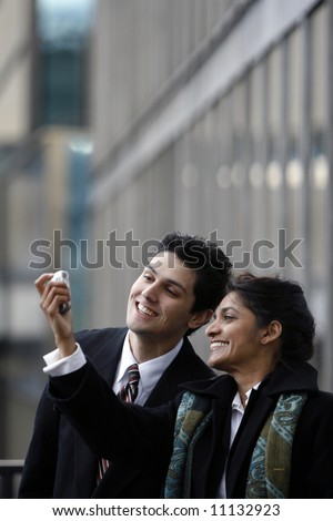 Indian business woman showing her male colleague something funny on her cell phone outside an office building