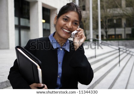 Executive Indian woman talking on a cellphone dressed in a black suit.