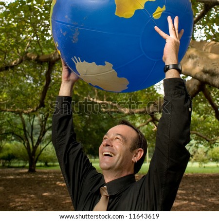 Latin American businessman standing in a grove of trees with an inflatable globe held above his head