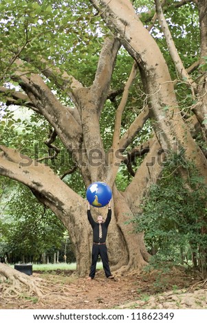 Latin american business man standing in front of a huge tree with a globe held over his head in his outstretched hands