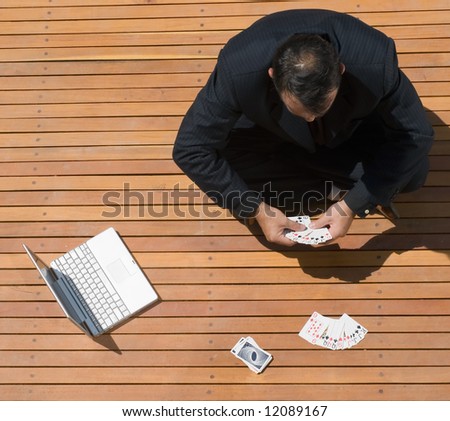 Latin american business man sitting cross legged with playing cards and his laptop computer in front of him