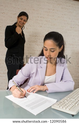 Latin american business woman pumping her fist as another woman in the foreground signs a contract
