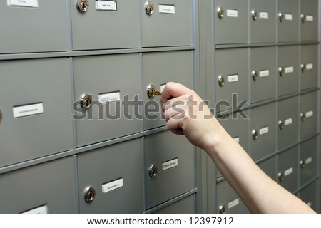 Close up of a hand putting a key into a lock in a row of mailboxes or safety deposit boxes