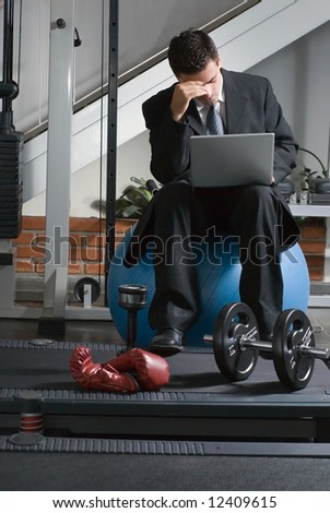 A shot of a business, at the gym, using a laptop with a frustrated look on his face.