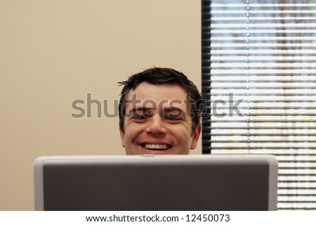 Businessman sitting behind a laptop screen with a broad smile on his face. Horizontally framed shot