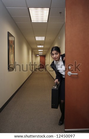 Businesswoman looking around suspiciously with a briefcase in hand in an empty hallway