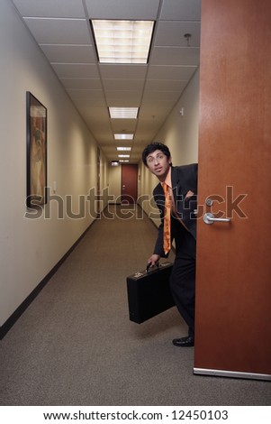Businessman looking around suspiciously with his briefcase in hand in an empty hallway