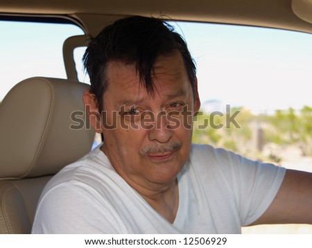 An isolated shot of an older man driving a SUV in the desert.