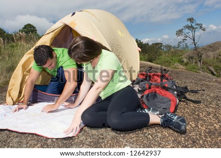 Young couple checking their route on a map in front of their tent with ominous gray clouds gathering overhead. Horizontally framed shot.