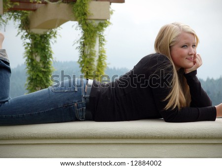 Cute blond woman relaxing in the sunshine relaxing on a stone wall with a blue sky in the background