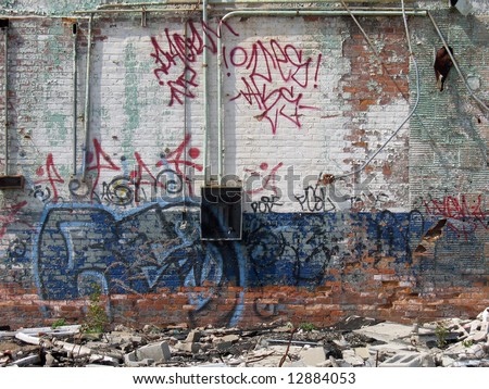 A graffiti covered wall of an abandoned brick building, which is painted white and blue.