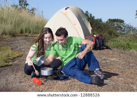 Attractive young couple cooking a meal while on a camping trip. Horizontally framed shot set against a clear blue sky