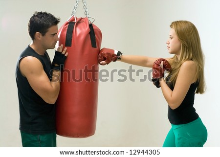 Attractive woman working out with boxing gloves and a heavy punching bag with her trainer.