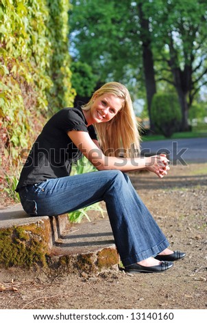 Attractive young blond woman casually dressed smiling at the camera sitting on some stone steps in golden evening light