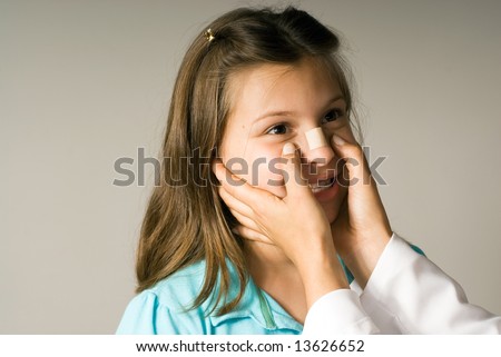 Young girl smiles while a band-aid is applied to her nose. She is happy to be taken care of. Horizontally framed photograph