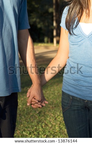 Close up of the arms of two people holding hands in a park. Vertically framed photograph