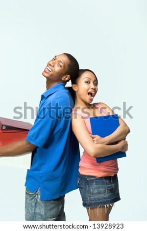 Two teenagers standing back to back holding notebooks are smiling and being silly. Vertically framed photograph