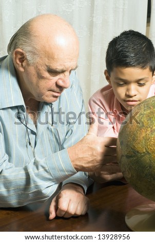 Grandfather and Grandson are seated at a table looking at a globe together. Vertically framed photograph.