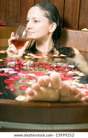 Woman relaxes in a spa tub filled with flowers sips red wine. Vertically framed photograph