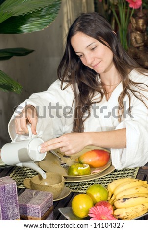 Woman pours tea while having breakfast surrounded by candles and fruit. Vertically framed photograph