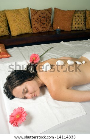 Woman closes her eyes and relaxes as she gets a hot stone massage. Vertically framed photograph.