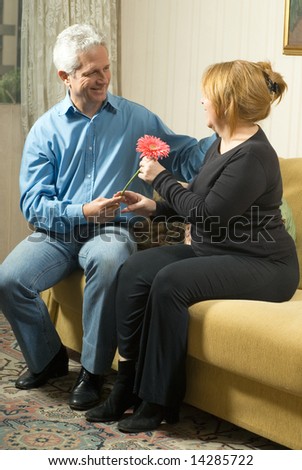 Happy older couple, the man is presenting a flower to the woman, she is smiling and accepting the flower. Vertically framed shot.
