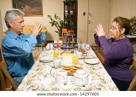A couple making hand gestures towards each other at a dinner table. - horizontally framed