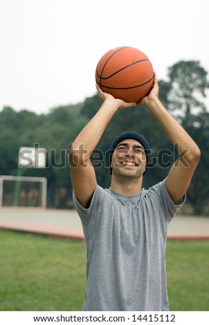 A man, in a park, stands tall, ready to shoot a basketball while smiling - vertically framed