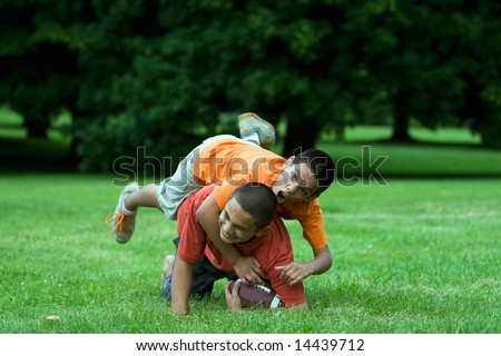 Two boys playing football in a field. One is tackling the other and they are laughing. Horizontally framed photograph.