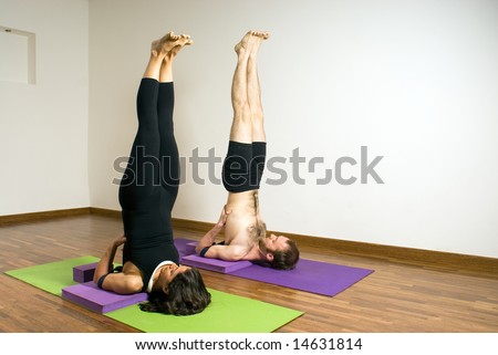 Man and woman in a yoga stretch, they are lying on mats with their feet up in the air. Vertically framed photograph